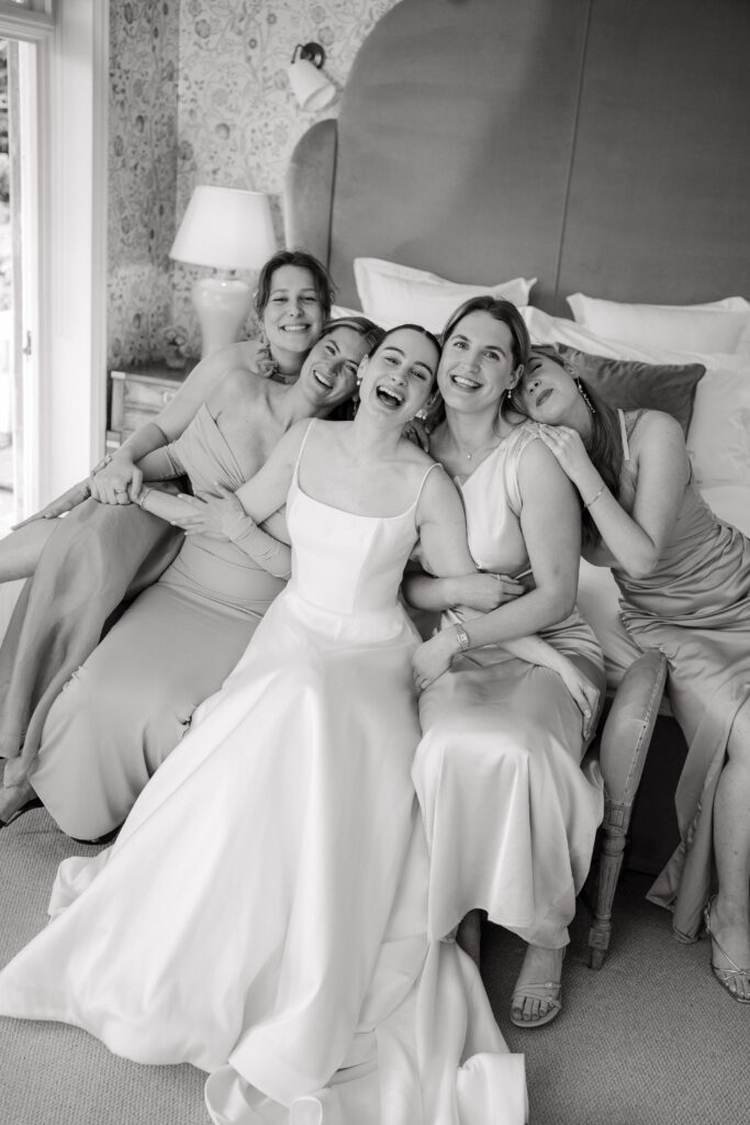 group photo of bridesmaids and bride laughing on the corner of the bed