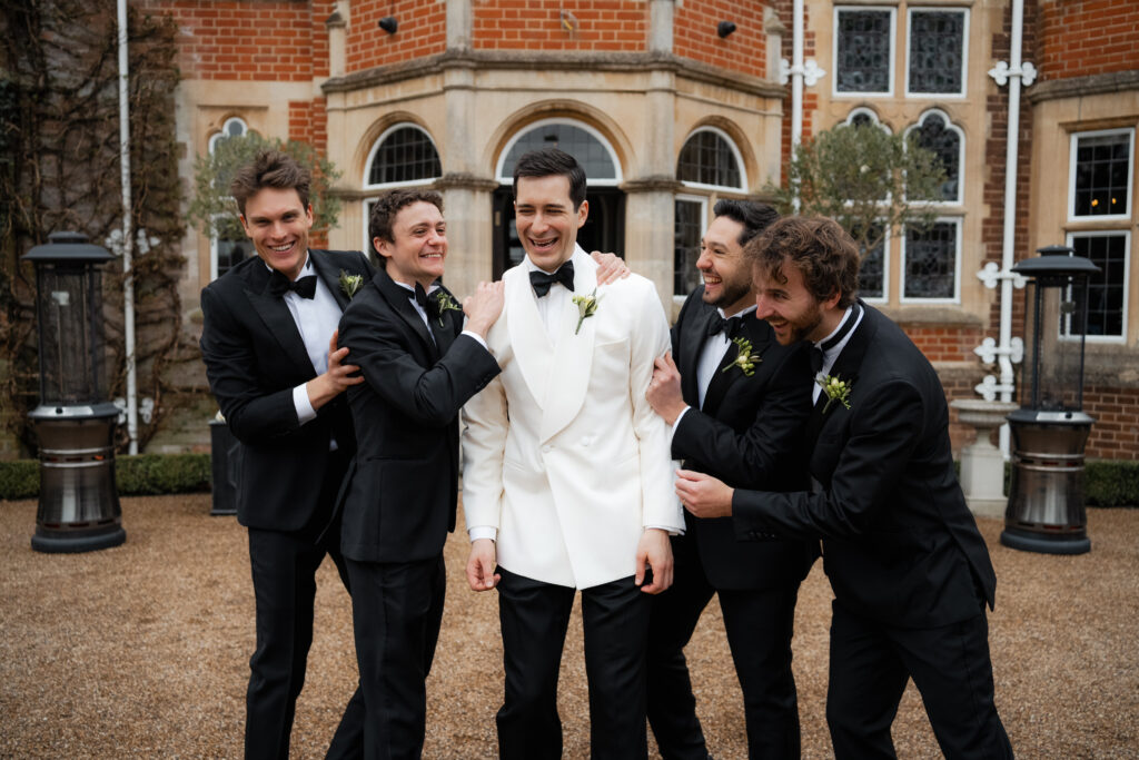 groom and groomsmen outside laughing and greeting guests